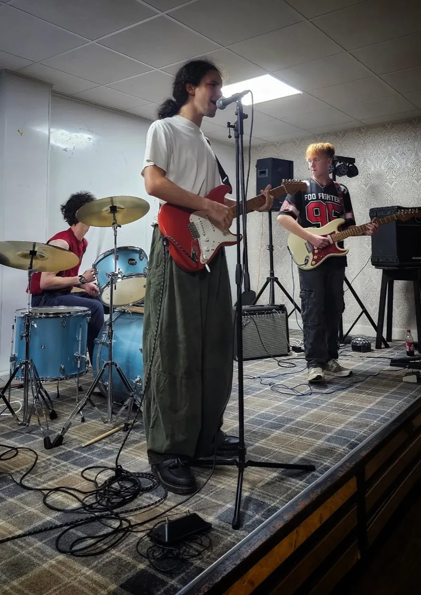 Rehearsing in a function room, vocals at the mic stand with drums behind